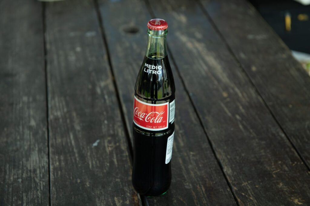 A classic Coca-Cola bottle placed on a rustic wooden table outdoors.