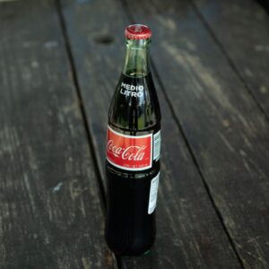 A classic Coca-Cola bottle placed on a rustic wooden table outdoors.