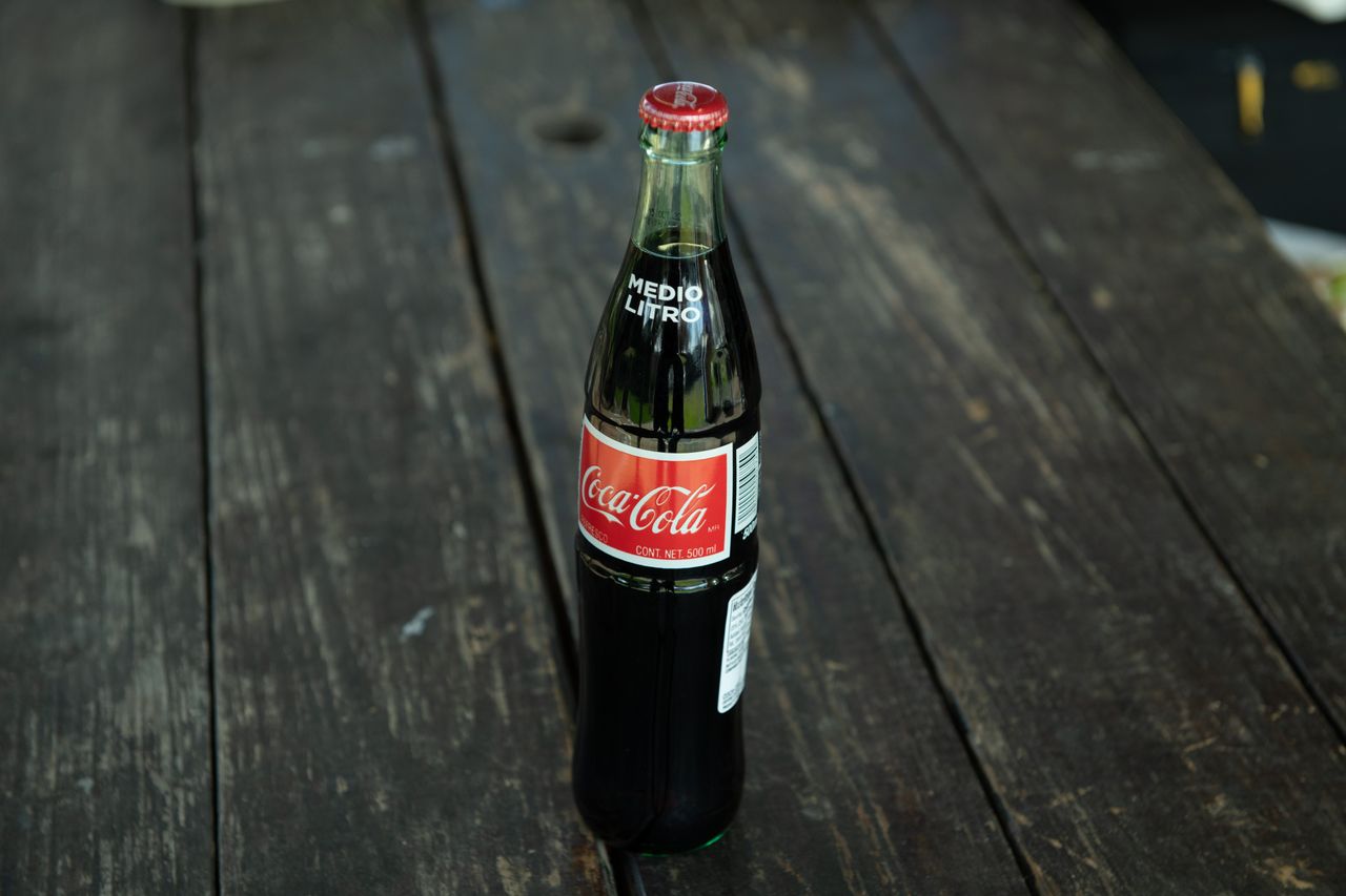 pexels-photo-29851093-29851093 A classic Coca-Cola bottle placed on a rustic wooden table outdoors.
