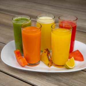 Colorful array of fresh fruit juices in glasses on a white plate with assorted fruits.