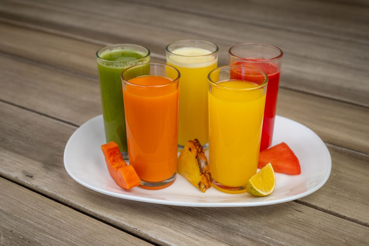 pexels-photo-31823004-31823004 Colorful array of fresh fruit juices in glasses on a white plate with assorted fruits.