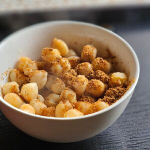 A white bowl filled with seasoned macadamia nuts on a dark table, creating an inviting snack scene.