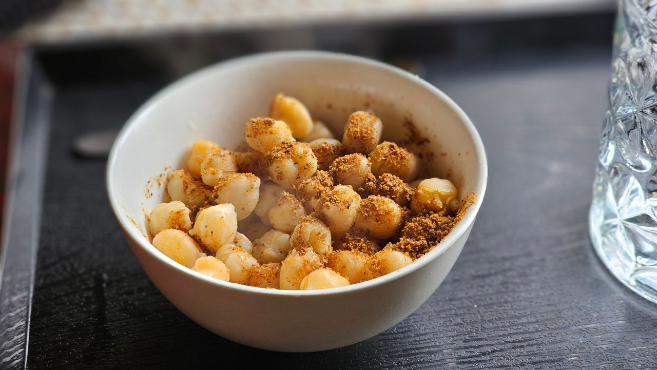 pexels-photo-36097108-36097108 A white bowl filled with seasoned macadamia nuts on a dark table, creating an inviting snack scene.