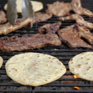 Close-up of sizzling meat and tortillas grilling on a barbecue, perfect for a delicious meal.